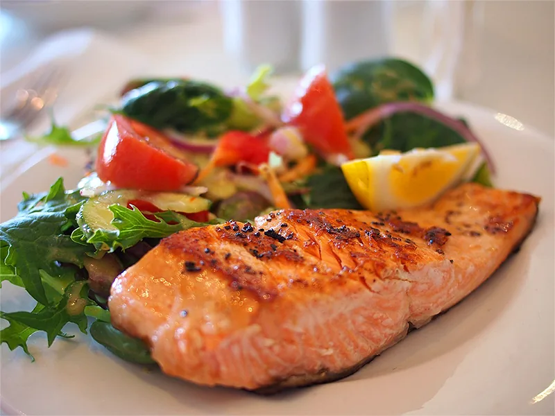 Grilled salmon fillet served with mixed salad and lemon wedge at Kaboso Safari Camp.