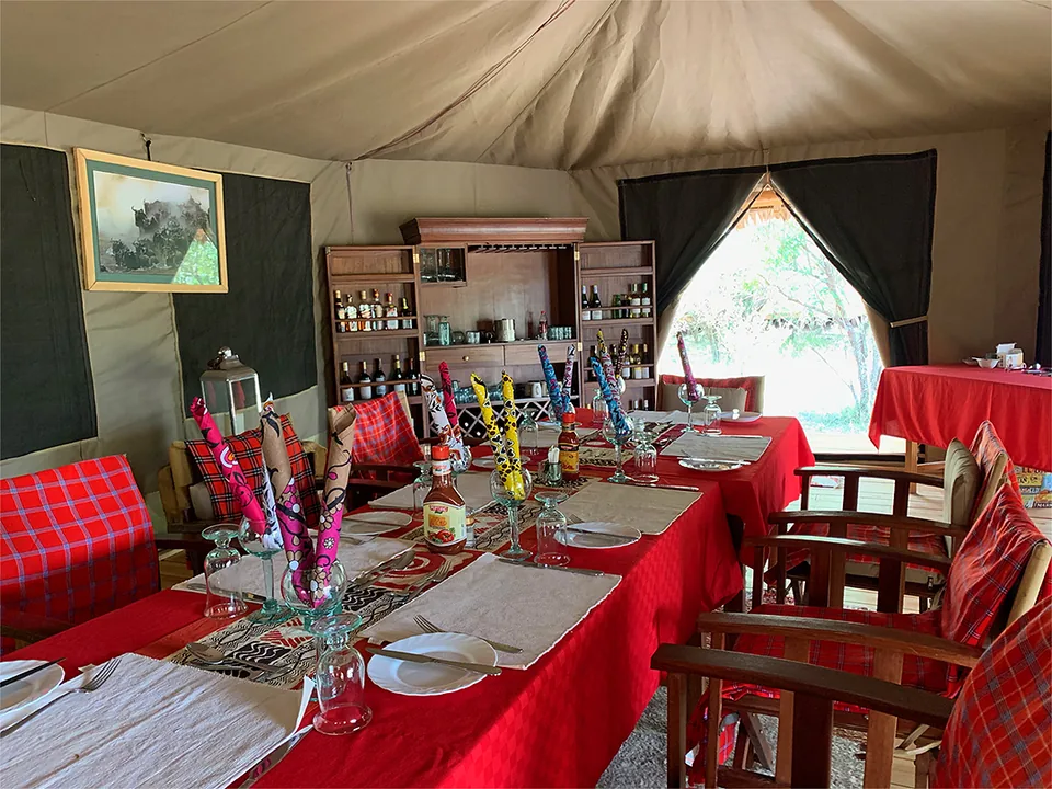 Dining setup inside a safari tent with red tablecloths and folded napkins at Kaboso Safari Camp.