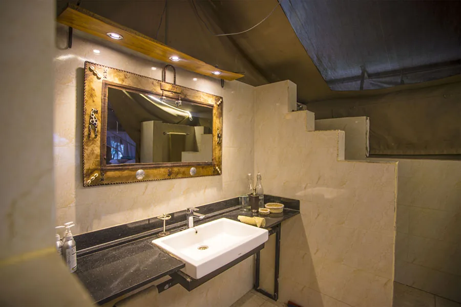 Tent-camp bathroom with sink, mirror, and stone counter at Kaboso Safari Camp.