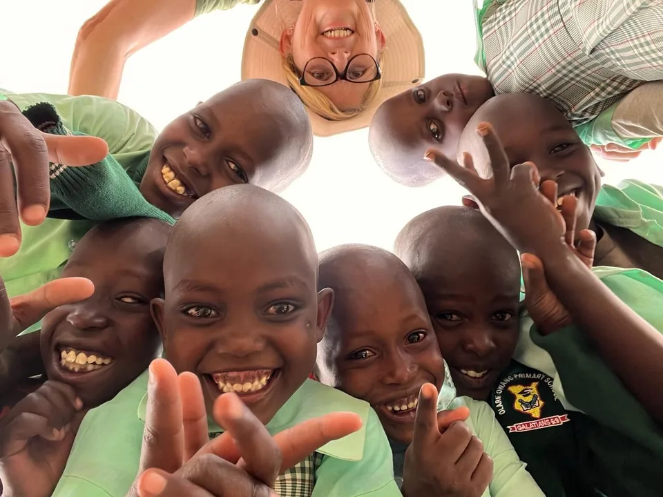 Group of children and one adult smiling around the camera from below.