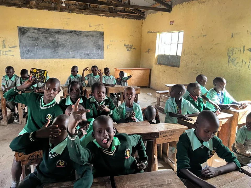 Classroom scene with children in green uniforms seated at wooden desks.